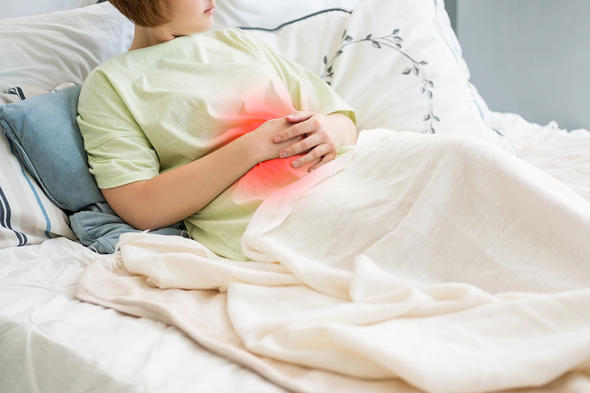 Woman lying in bed holding her lower abdomen while experiencing abdominal discomfort.