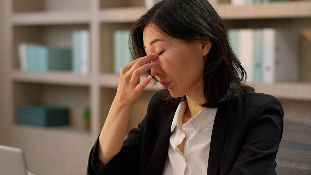 Woman with her eyes closed and fingers resting on the bridge of her nose while appearing fatigued.