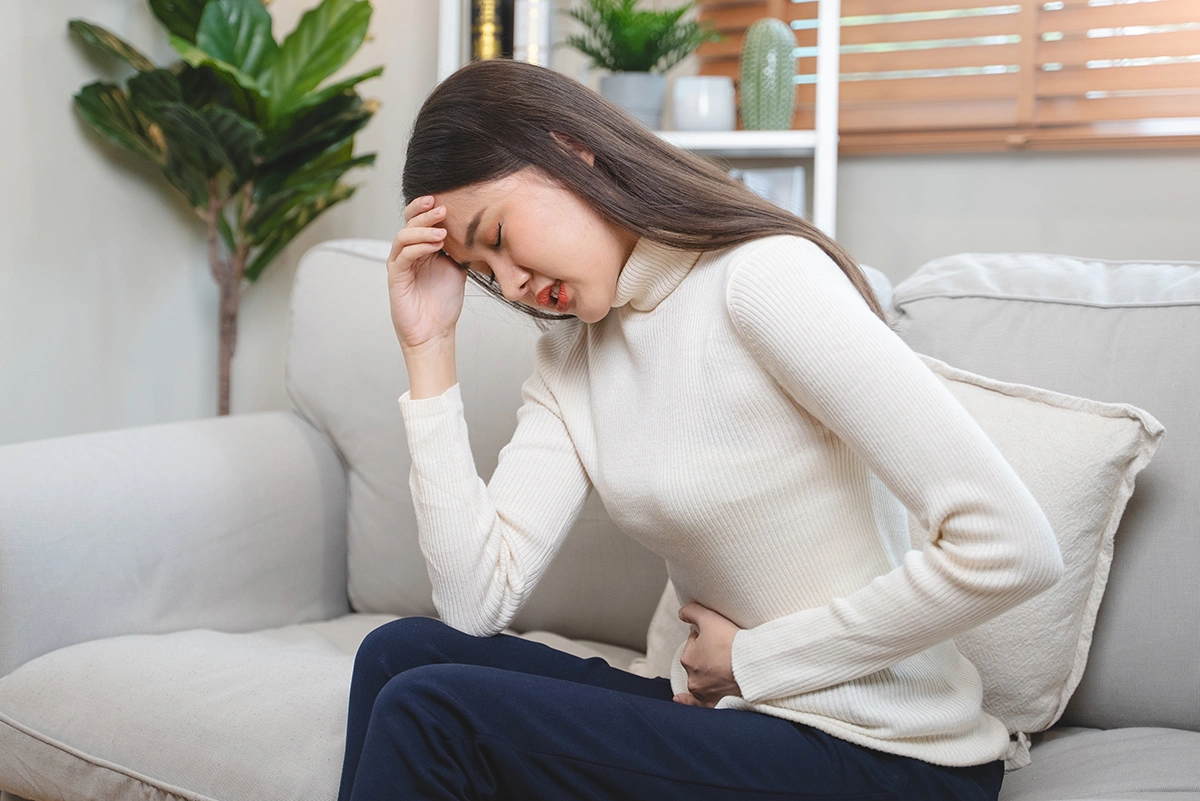 Woman seated and clutching her lower abdomen while experiencing pelvic discomfort.